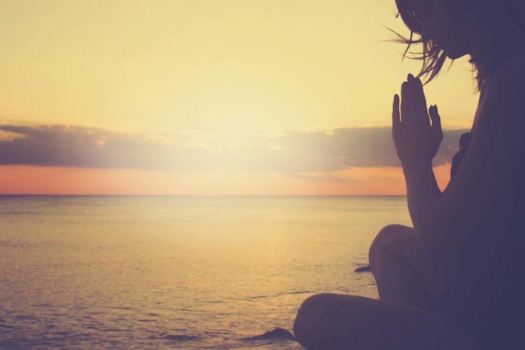 Chica meditando en la orilla del mar durante un atardecer