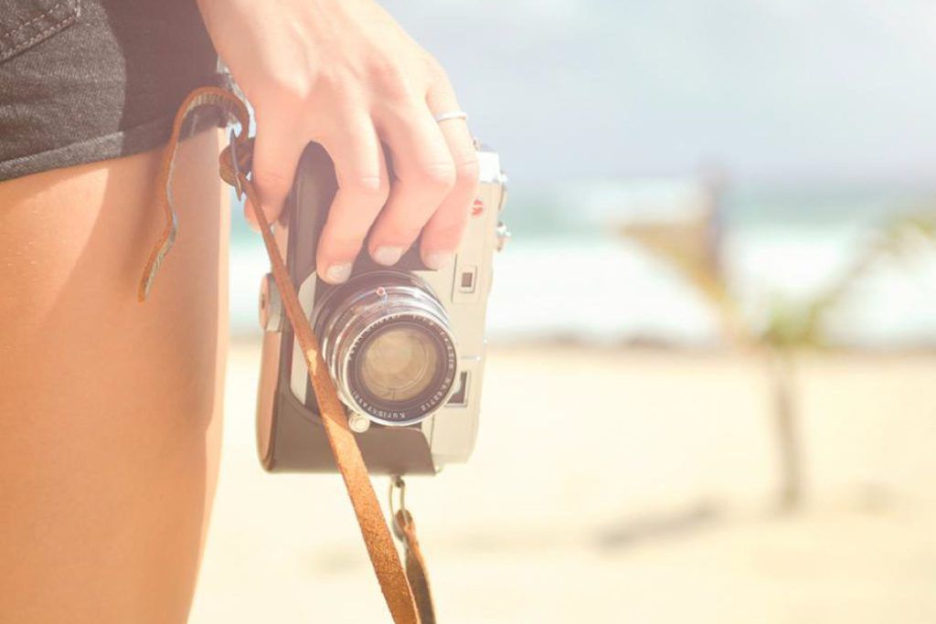Chica sujetando una cámara de fotos en una playa