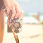 Chica sujetando una cámara de fotos en una playa