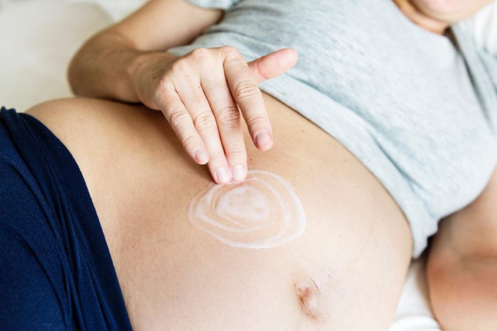 Mujer embarazada aplicando crema en la barriga