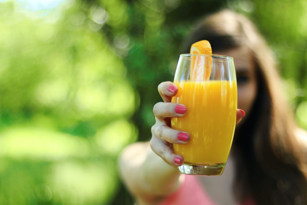 Chica en un jardín sujetando un vaso de zumo de naranja natural